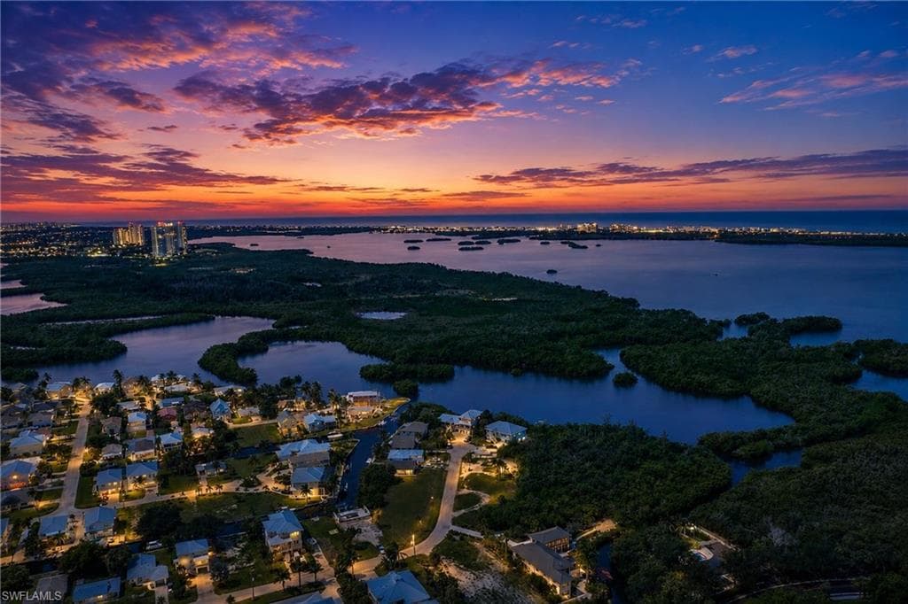 Coastal community featuring numerous homes with illuminated exteriors, water access, and mature natural landscaping