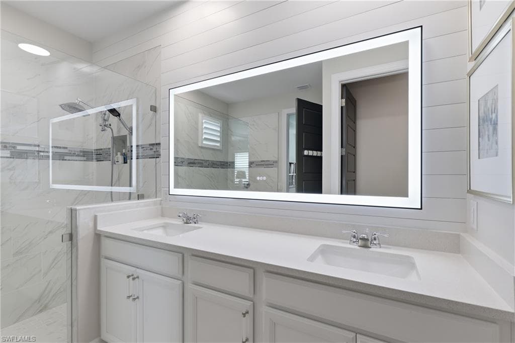 Spa-inspired owners bath with a dual vanity and frameless glass shower and elegant lighted mirror