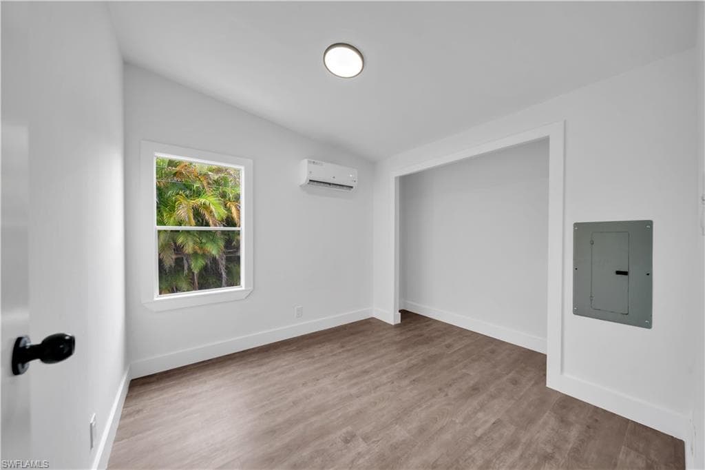 Bright interior space featuring wood-finish flooring, white walls, and a window with a tropical foliage backdrop