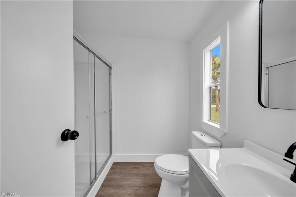 Bathroom featuring a glass-enclosed shower, wood-finish flooring, a contemporary vanity with an integrated sink, and a framed mirror