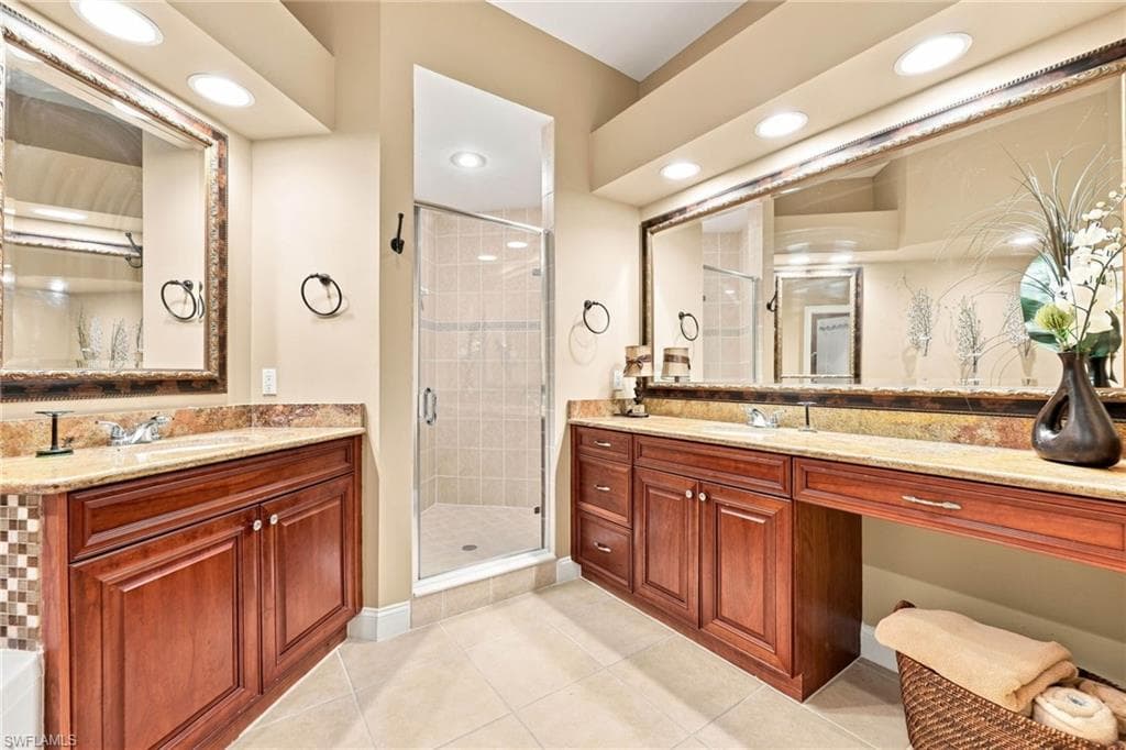 Luxurious primary bathroom featuring dual vanities with wood-finish cabinetry, granite countertops, and framed mirrors with integrated lighting