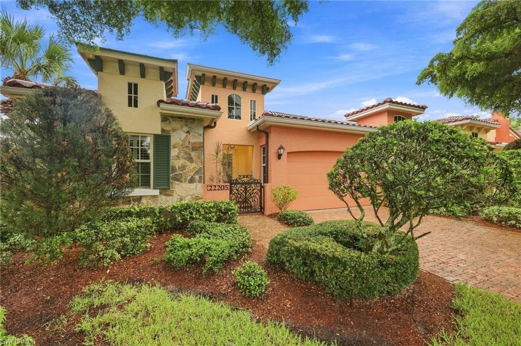 Mediterranean-style residence featuring stucco and stone veneer facade, a terracotta tile roof, and an attached garage with a paved driveway
