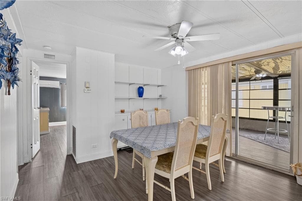 Dining area featuring wood-finish flooring, built-in shelving, a ceiling fan with integrated lighting, and sliding glass doors opening to an enclosed patio