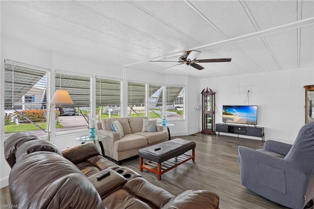 Spacious living area featuring expansive window treatments, wood-finish flooring, and a ceiling fan