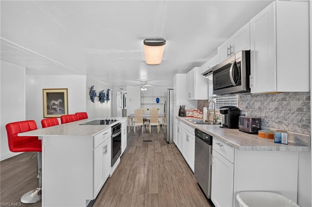 Open-concept kitchen featuring white cabinetry, a large kitchen island with cooktop, stainless steel appliances, wood-finish flooring, and a textured tile backsplash