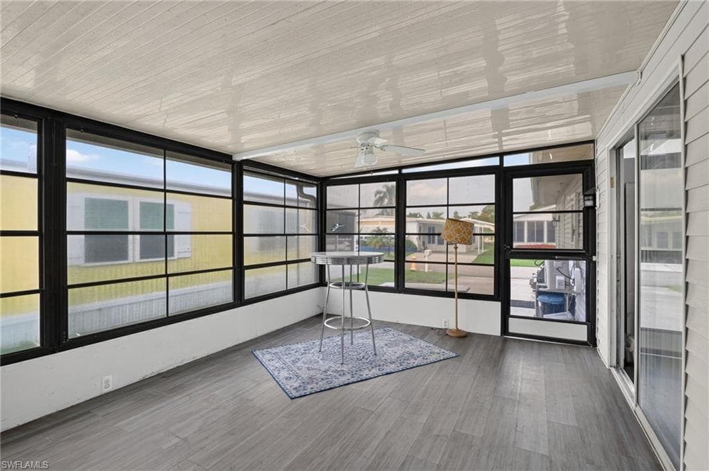Enclosed sunroom featuring a ceiling fan, wall-to-wall windows with black frames, and wood-finish flooring