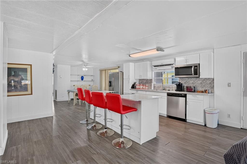 Kitchen featuring white cabinetry, stainless steel appliances, a white island, and wood-finish flooring