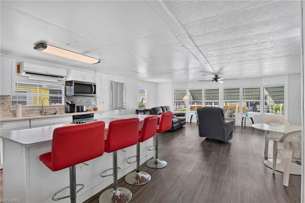 Open-concept living area featuring a kitchen island with seating, dark wood-finish flooring, white cabinetry, a tiled backsplash, and recessed lighting