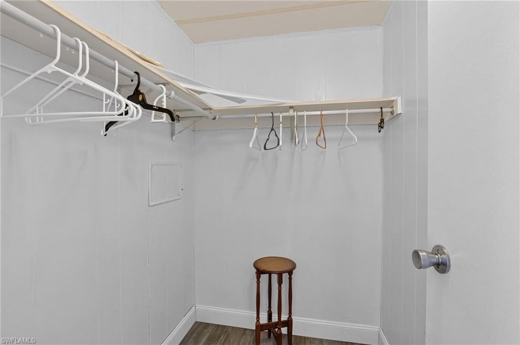 L-shaped closet with white paneled walls, wood-finish flooring, and a white door with a brushed nickel knob