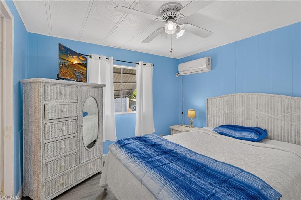 Bedroom featuring paneling walls, a ceiling fan with integrated lighting, and a wall-mounted mini-split AC unit