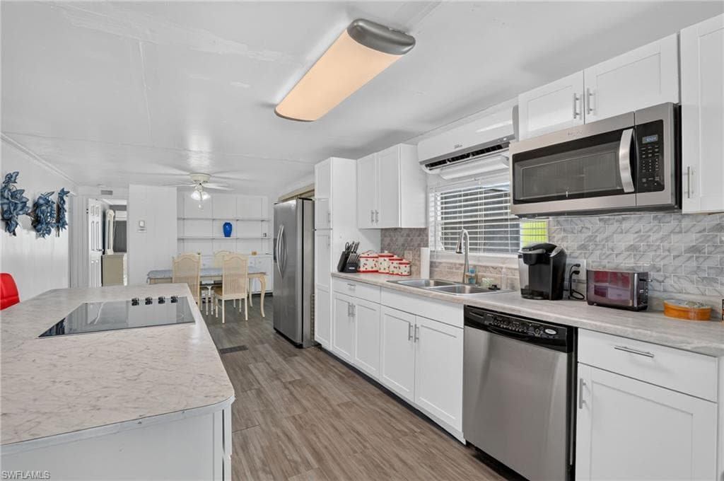 Spacious kitchen featuring white cabinetry, light countertops, wood-finish flooring, a stainless steel appliance suite, and a tile backsplash