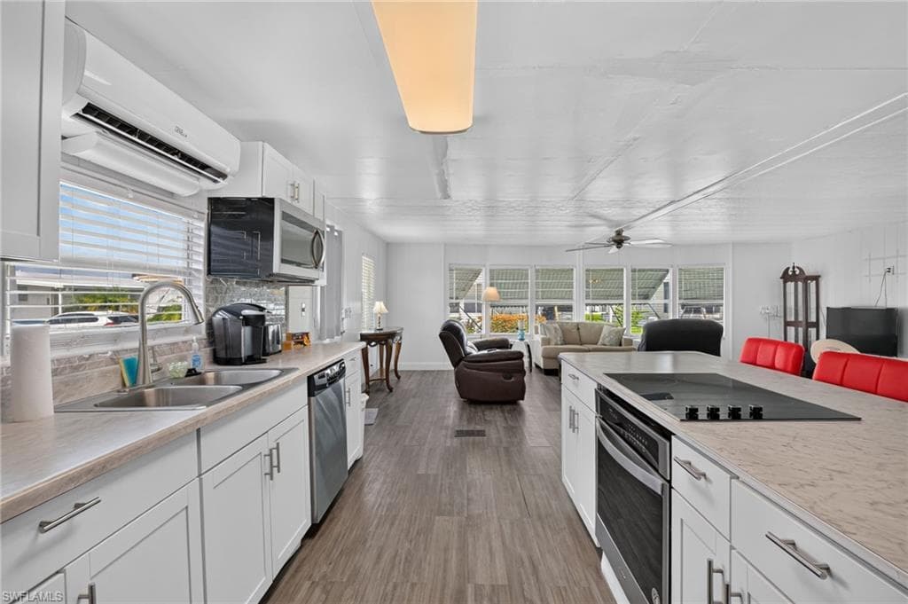 Open-concept kitchen featuring white cabinetry, stone-finish countertops, stainless-steel appliances, and wood-finish flooring