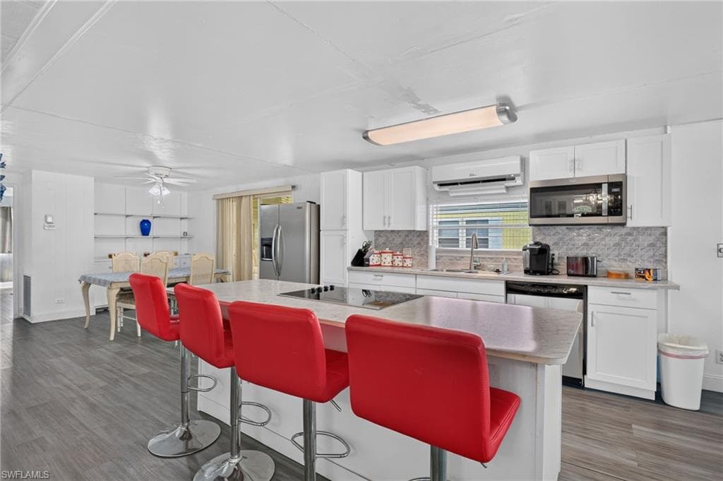 Open-concept kitchen and dining area featuring white cabinetry, gray wood-finish flooring, a kitchen island with seating, stainless steel refrigerator, and a built-in microwave