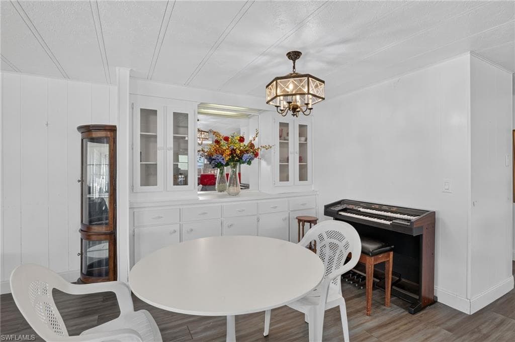 Spacious interior featuring built-in cabinetry with glass-front uppers, a functional ceiling light fixture, wood-finish flooring, and white paneled walls