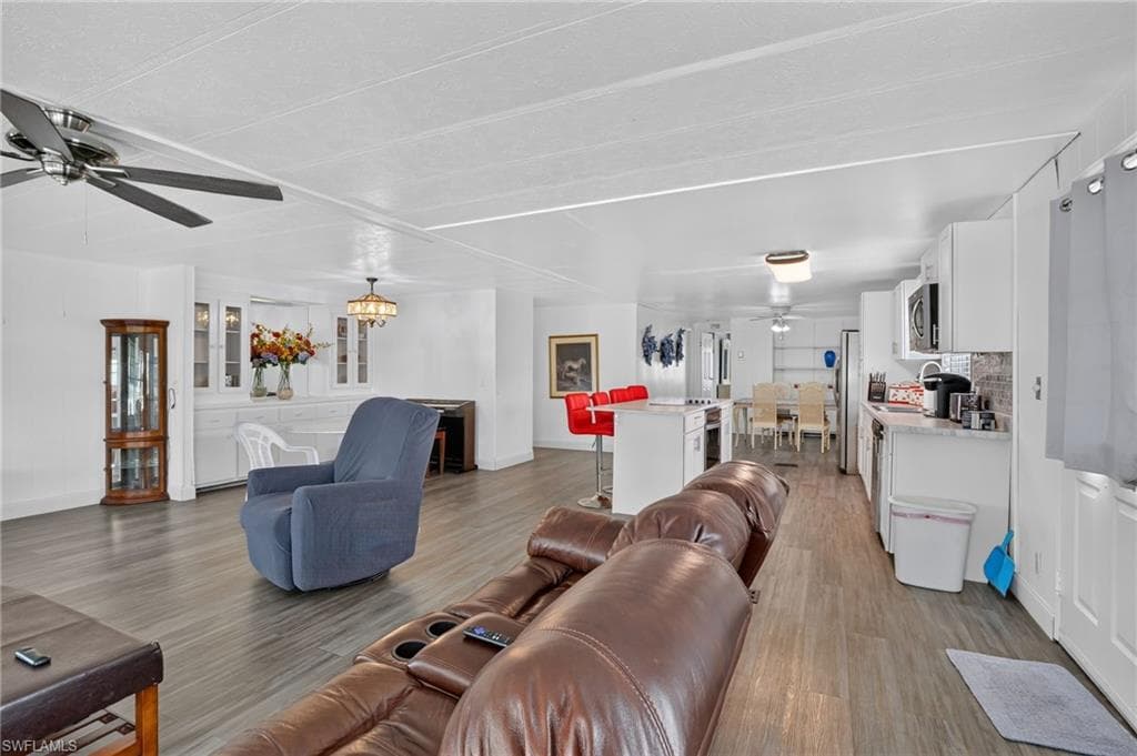 Open-concept interior featuring wood-finish flooring, white cabinetry, a built-in buffet with glass-front cabinets, and a kitchen island with a breakfast bar