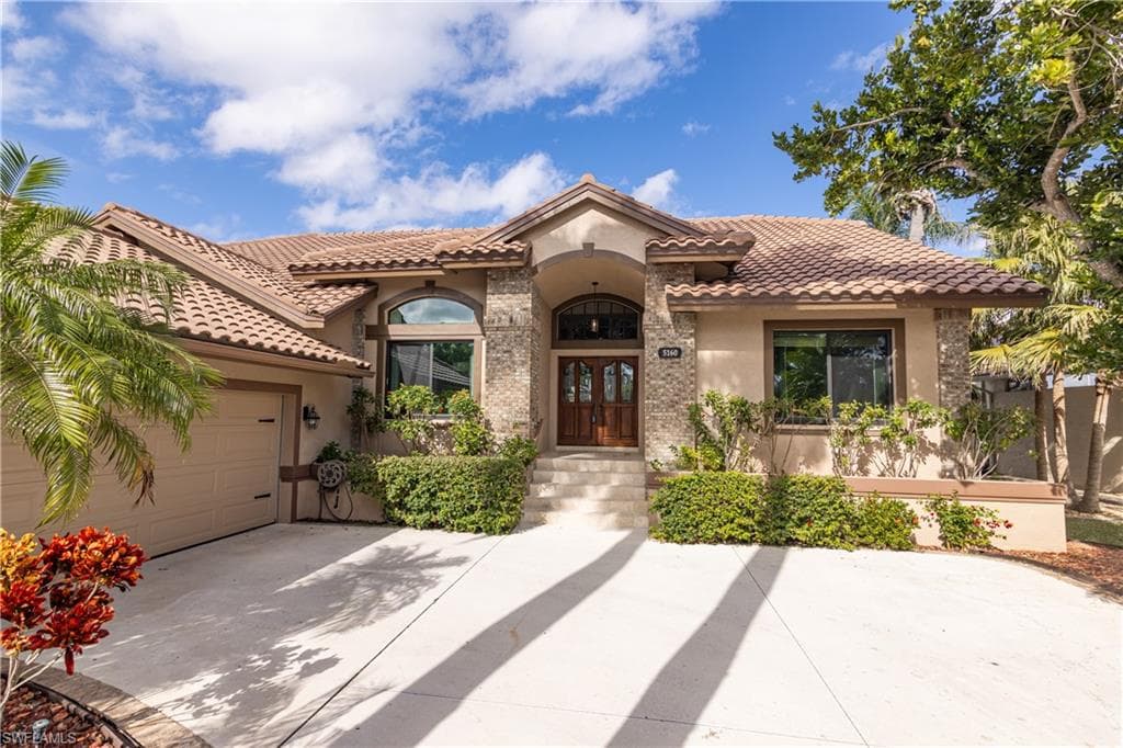 Mediterranean-style residence featuring a tile roof, stucco exterior, stone accents, and a double wood-finish entry door with an arched transom