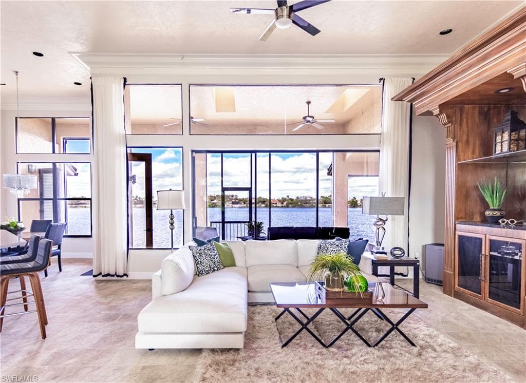 Expansive living area featuring floor-to-ceiling windows, waterfront views, a built-in wood-finish cabinet with glass doors, recessed lighting, and a ceiling fan