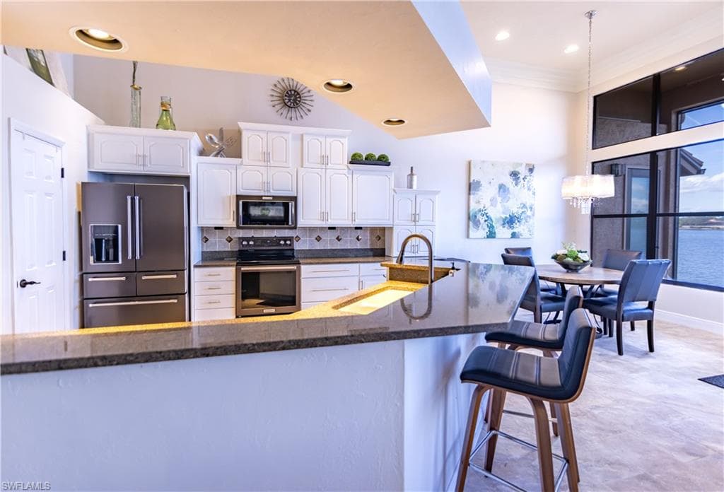Kitchen featuring white cabinetry, stainless steel appliances, and a breakfast bar with stone-finish countertops
