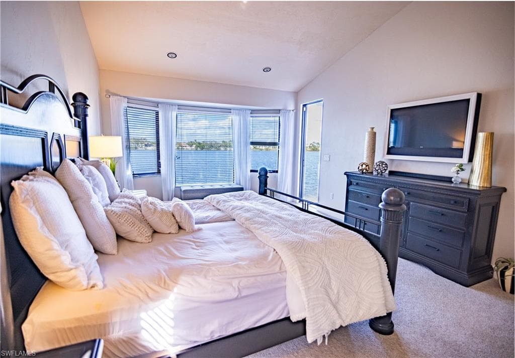 Bedroom featuring waterfront views, vaulted ceiling, recessed lighting, carpet flooring, and a bay window with integrated seating