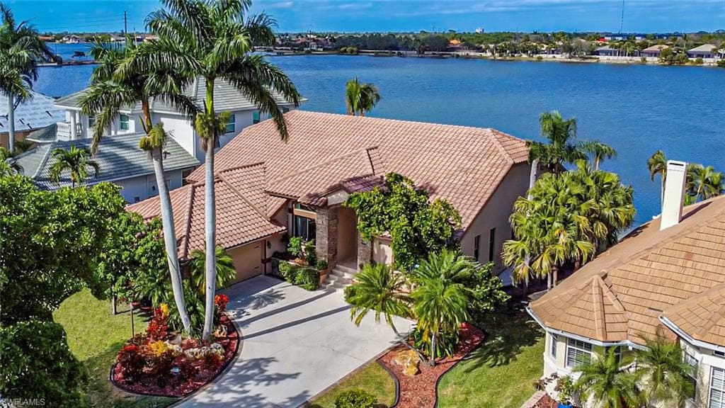 Waterfront residence featuring a barrel tile roof, arched entryway with decorative columns, and mature palm landscaping