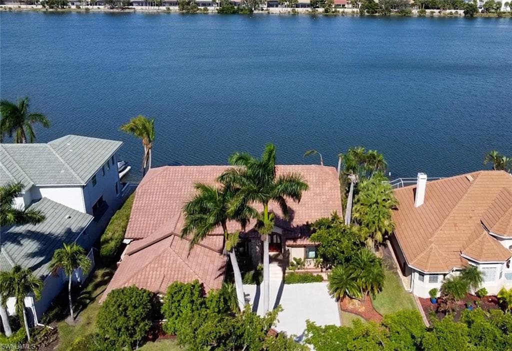 Waterfront property featuring a tile roof, mature palm trees, a concrete driveway, and established landscaping