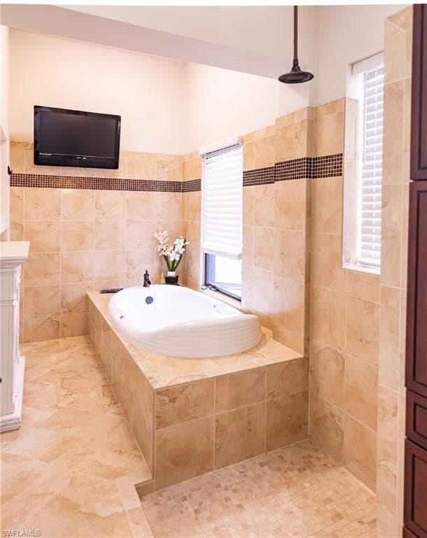 Tiled bathroom featuring a built-in soaking tub, a rain shower head, and an integrated wall-mounted television