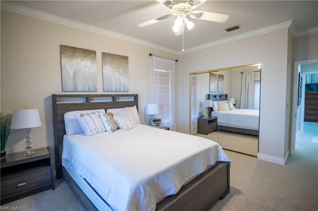 Carpeted bedroom featuring a ceiling fan with integrated lighting, crown molding, and a full-height mirrored closet