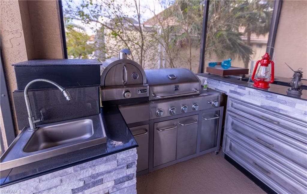 Outdoor kitchen featuring a stainless steel grill with multiple burners, an integrated pizza oven, and a stainless steel sink with a gooseneck faucet