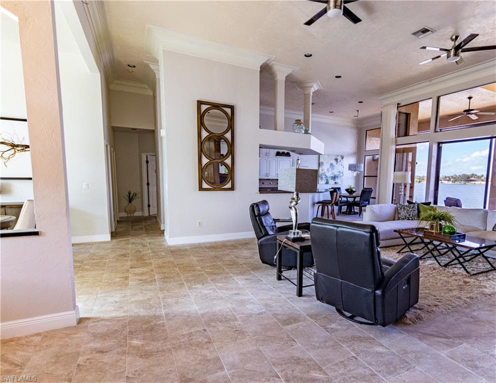 Open-concept living area featuring large format tile flooring, crown molding, and extensive window views of the waterway