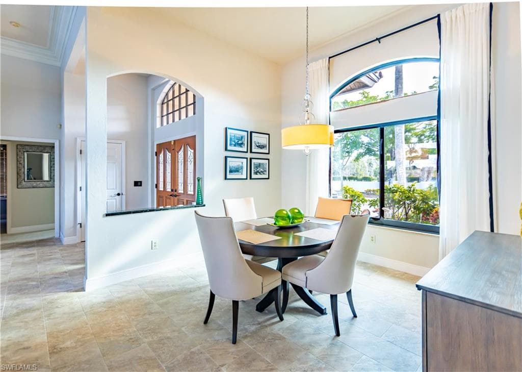 Bright interior space featuring large arched windows with white drapery, neutral-toned tile flooring, and a contemporary chandelier