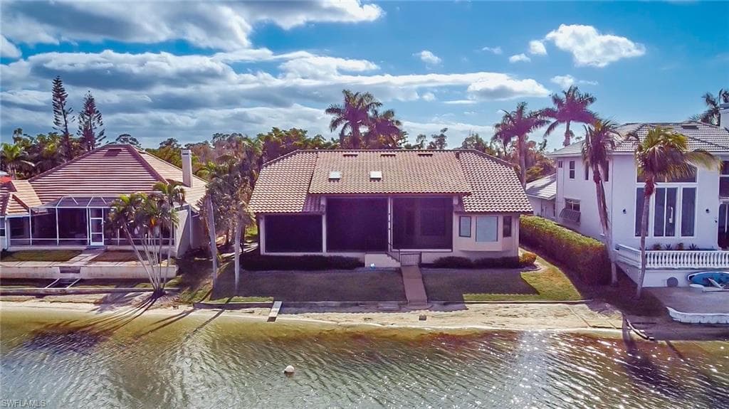 Waterfront property featuring a tile roof, screened patio, palm trees, and an established lawn
