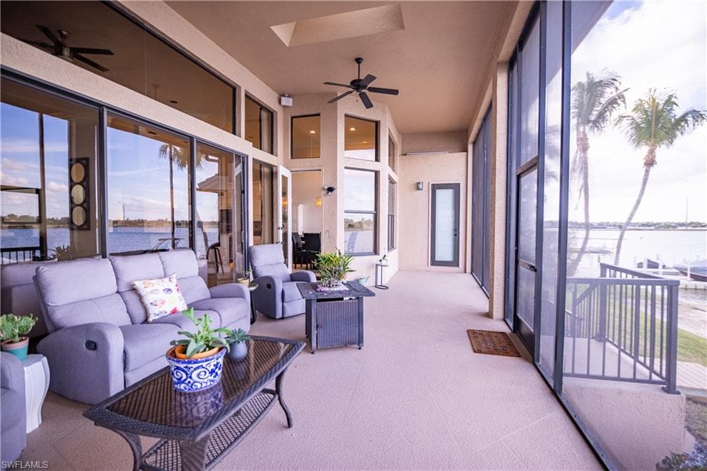 Spacious screened lanai featuring extensive glass sliding doors, water frontage, dual ceiling fans, and a balcony with metal railings