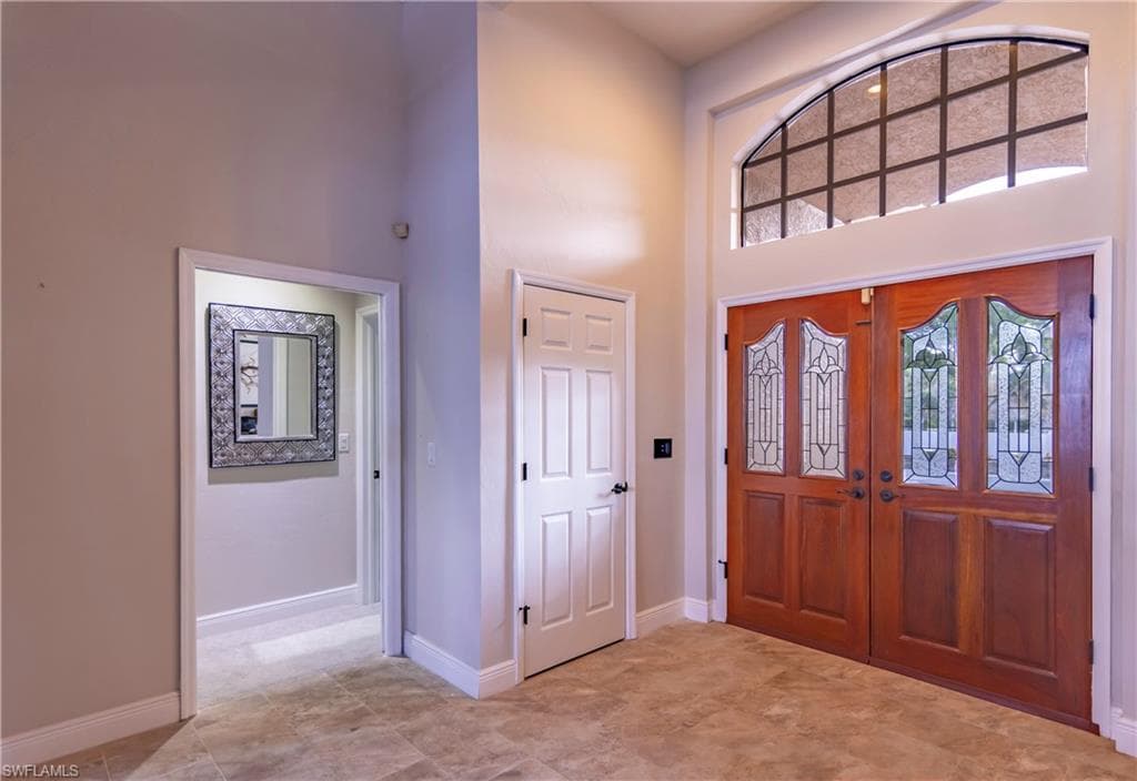 Grand entryway featuring double wood doors with decorative glass inserts, a high arched transom window, and tile flooring