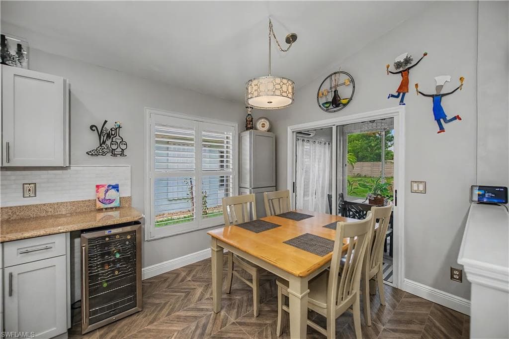 Kitchen dining area featuring a vaulted ceiling with a decorative pendant light, wood-finish flooring in a herringbone pattern, and white cabinetry with a light-colored countertop