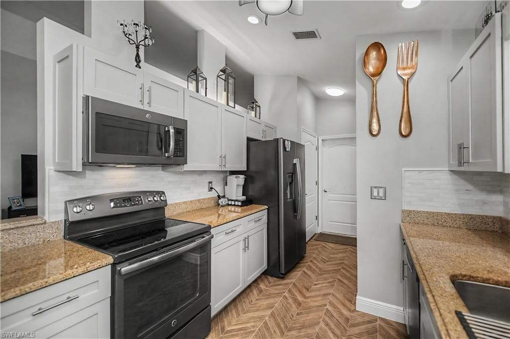 Galley kitchen featuring light-toned cabinetry, light-colored countertops, stainless steel appliances, and wood-finish flooring