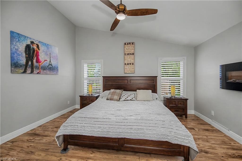 Vaulted ceiling with a wood-finish ceiling fan, wood-finish flooring, and white baseboards