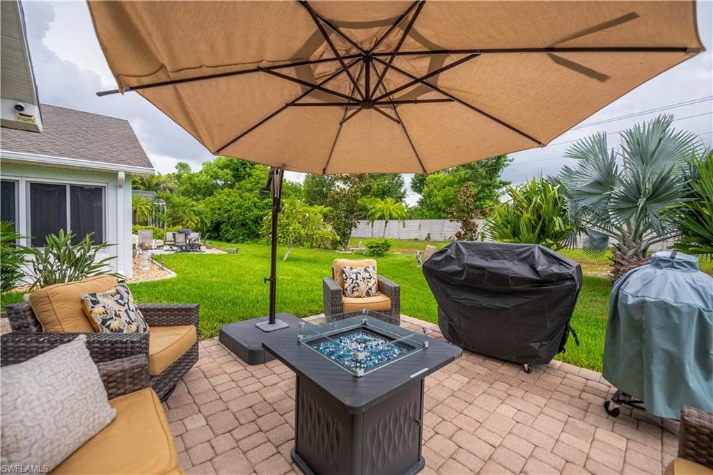 Brick paver patio featuring a fire pit table with blue glass accents, wicker-style outdoor seating, and a large umbrella