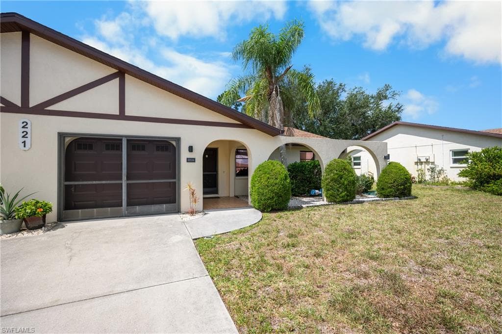 Exterior featuring a stucco facade with decorative timber accents, an attached garage with a screen door, and a covered entryway with an arched design