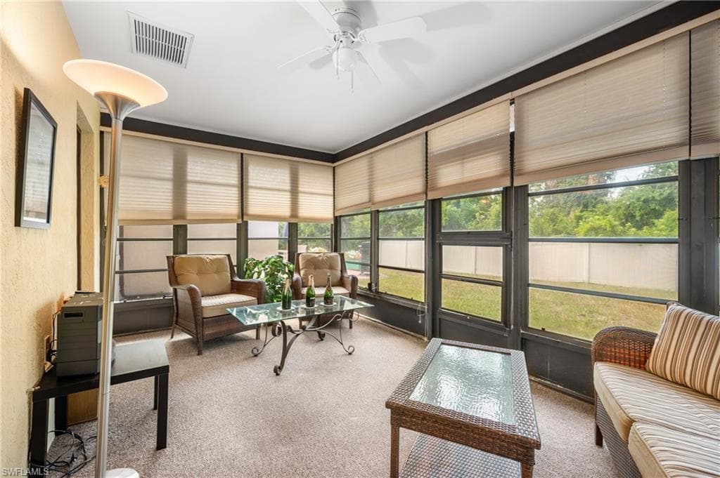 Enclosed sunroom featuring multiple large windows with blinds, a ceiling fan, and carpet flooring