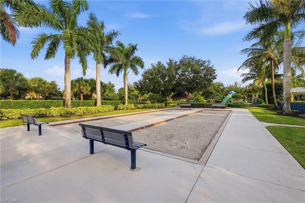 Expansive recreational grounds featuring a regulation horseshoe pit with two benches, wide concrete pathways, and mature landscaping including towering palms and established shade trees throughout the manicured lawn