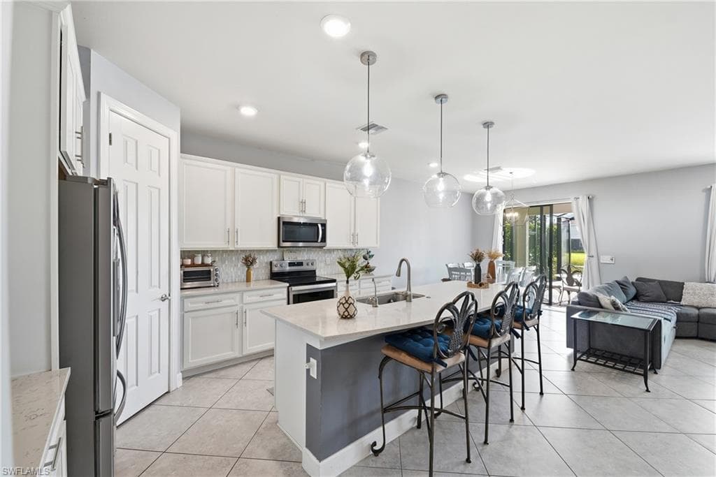 Open-concept kitchen featuring white cabinetry, stainless steel appliances, and a central island with a sink