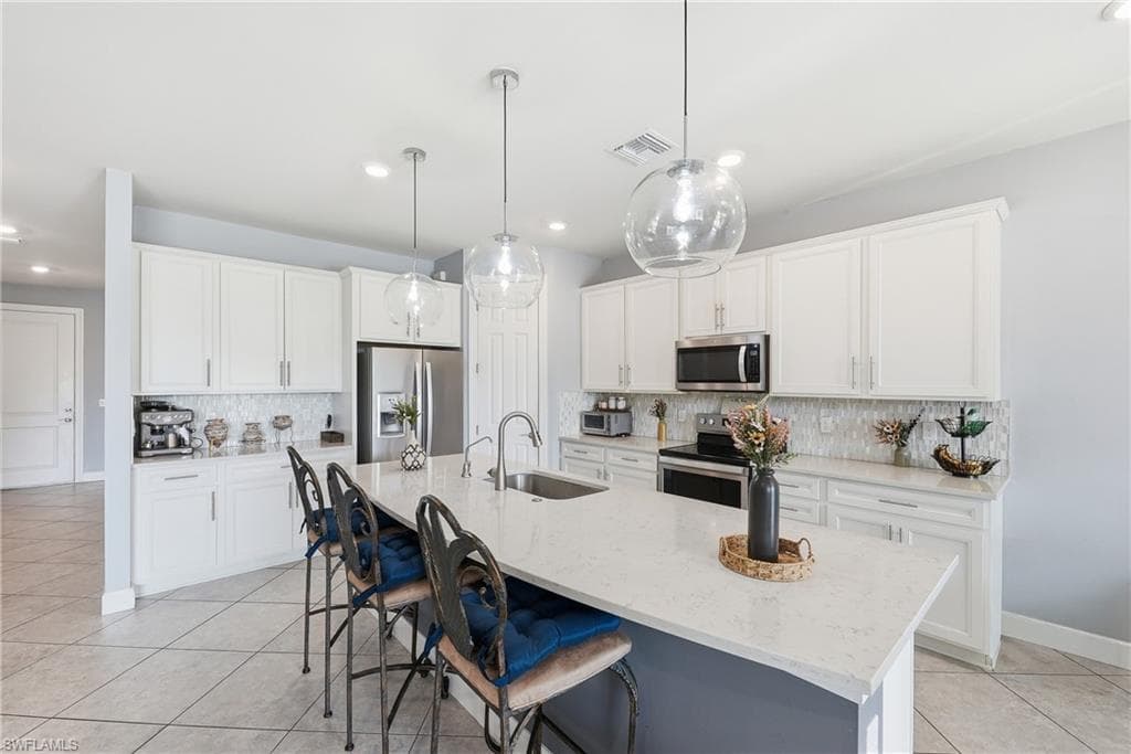 Spacious kitchen featuring an expansive island with a waterfall countertop, white shaker-style cabinetry, stainless steel appliances, a mosaic tile backsplash, and contemporary pendant lighting