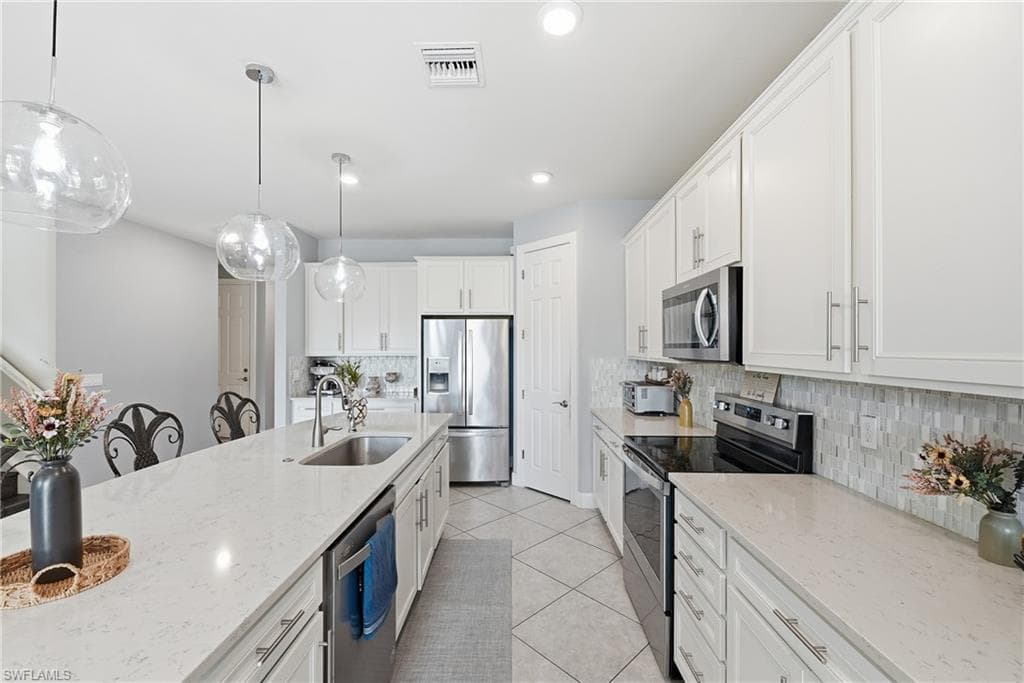 Kitchen featuring white cabinetry, stainless steel appliances, a long center island with an undermount sink, pendant lighting, and light-toned countertops