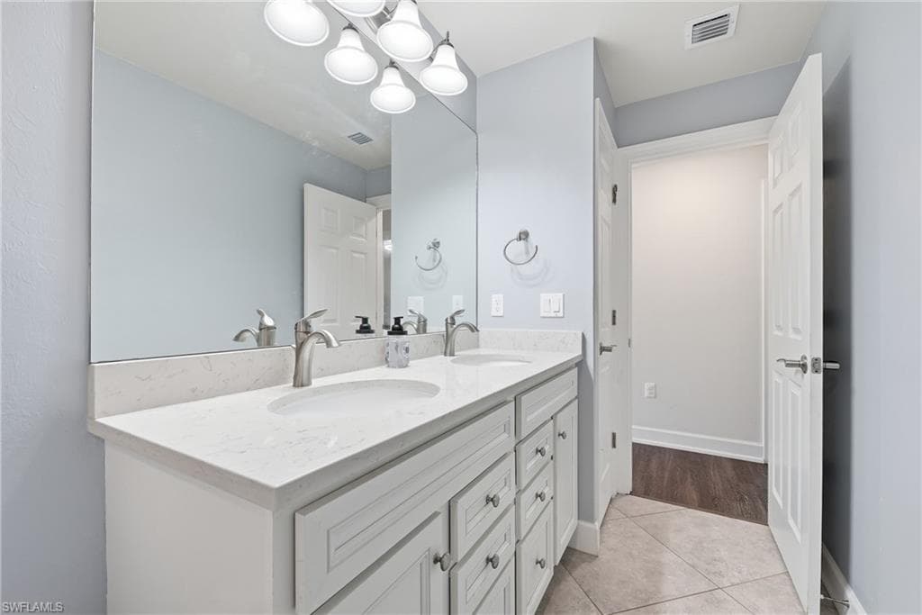 Bathroom featuring a dual-sink vanity with a light-toned countertop, integrated sinks, white cabinetry, and brushed nickel fixtures