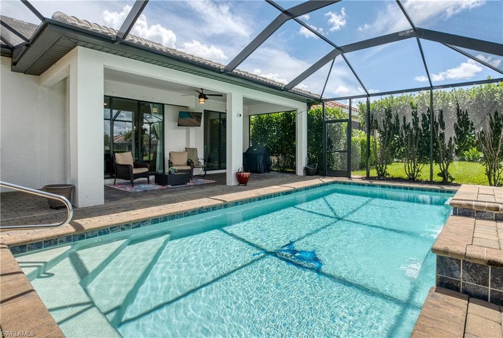 Screened enclosure featuring a rectangular pool with integrated steps, surrounded by brick-patterned pavers and a tiled water line