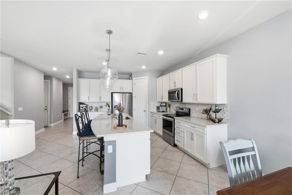 Modern kitchen featuring a large curved island, recessed lighting, white cabinetry, stainless steel appliances, and a tiled backsplash