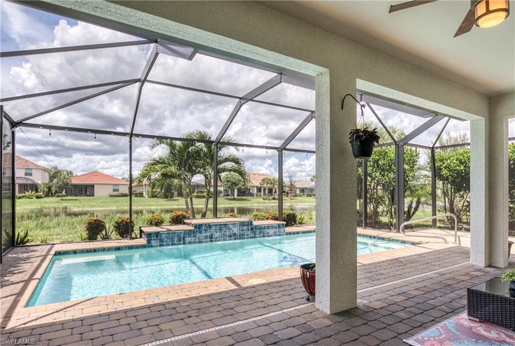 Screened lanai featuring a swimming pool, spa with a tile spillway, and paver decking