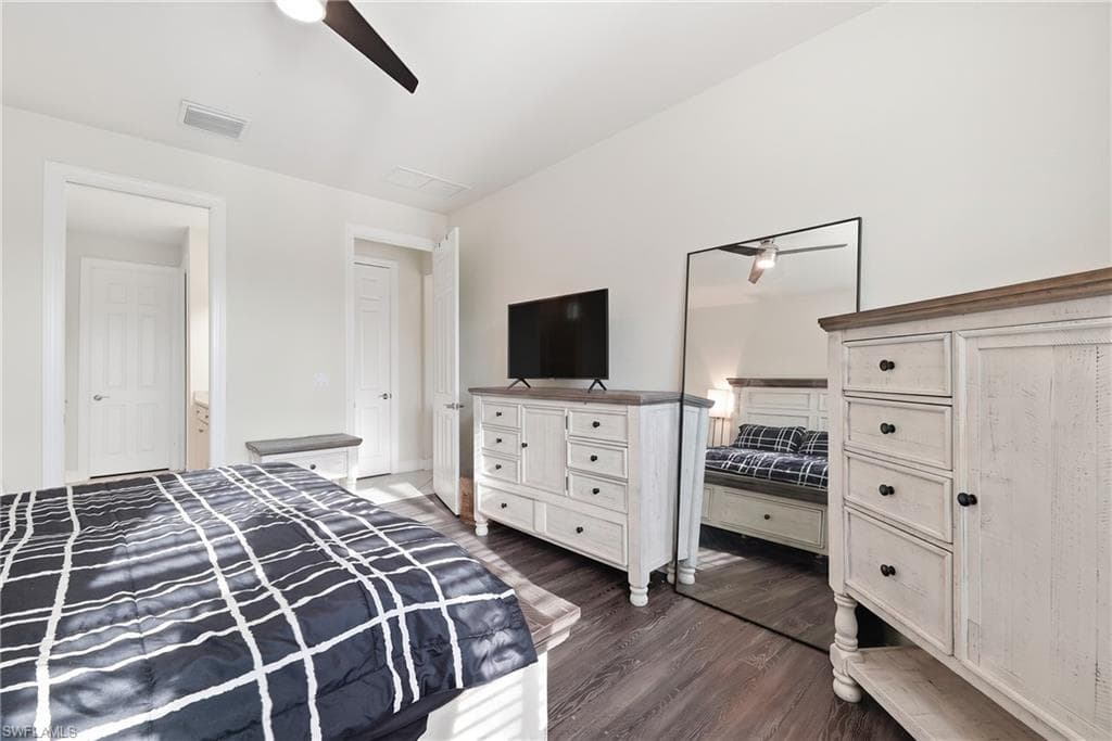 Spacious bedroom featuring hardwood flooring, white painted cabinetry with multiple drawers and storage, a flat-screen television mounted above a dresser, and coordinating furniture pieces