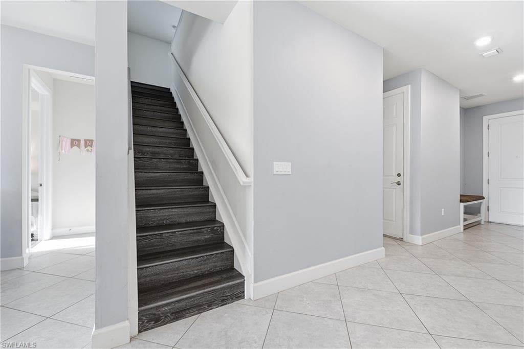 Wood-finish staircase with white handrail, light gray wall tones, white trim, and light-toned tile flooring throughout