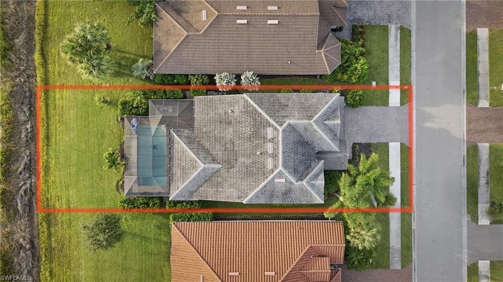 Aerial view showcasing the property's tile roof, screened pool enclosure, spacious green lawn, and paved driveway
